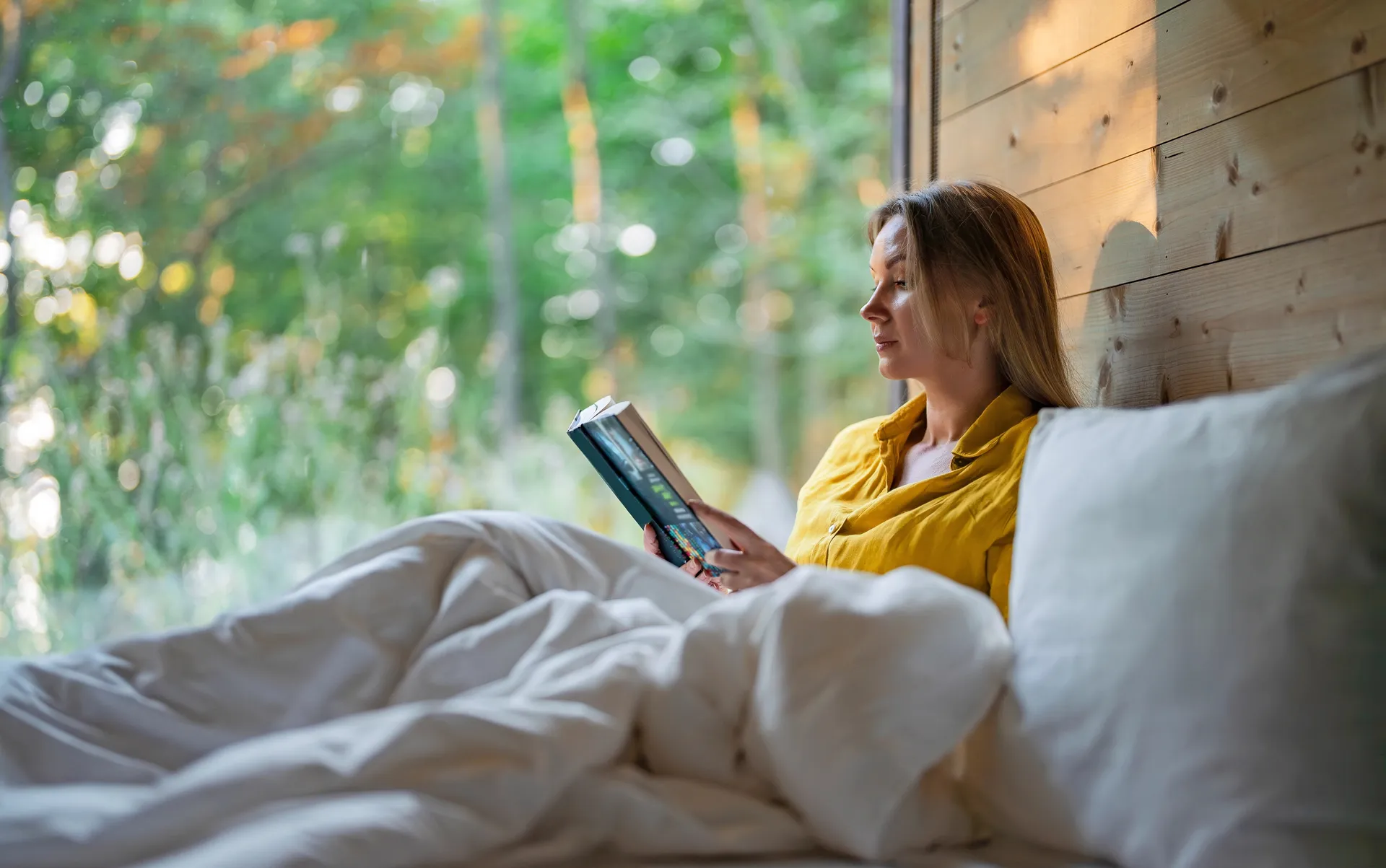 Guest reading in bed beside a large window onto woodland